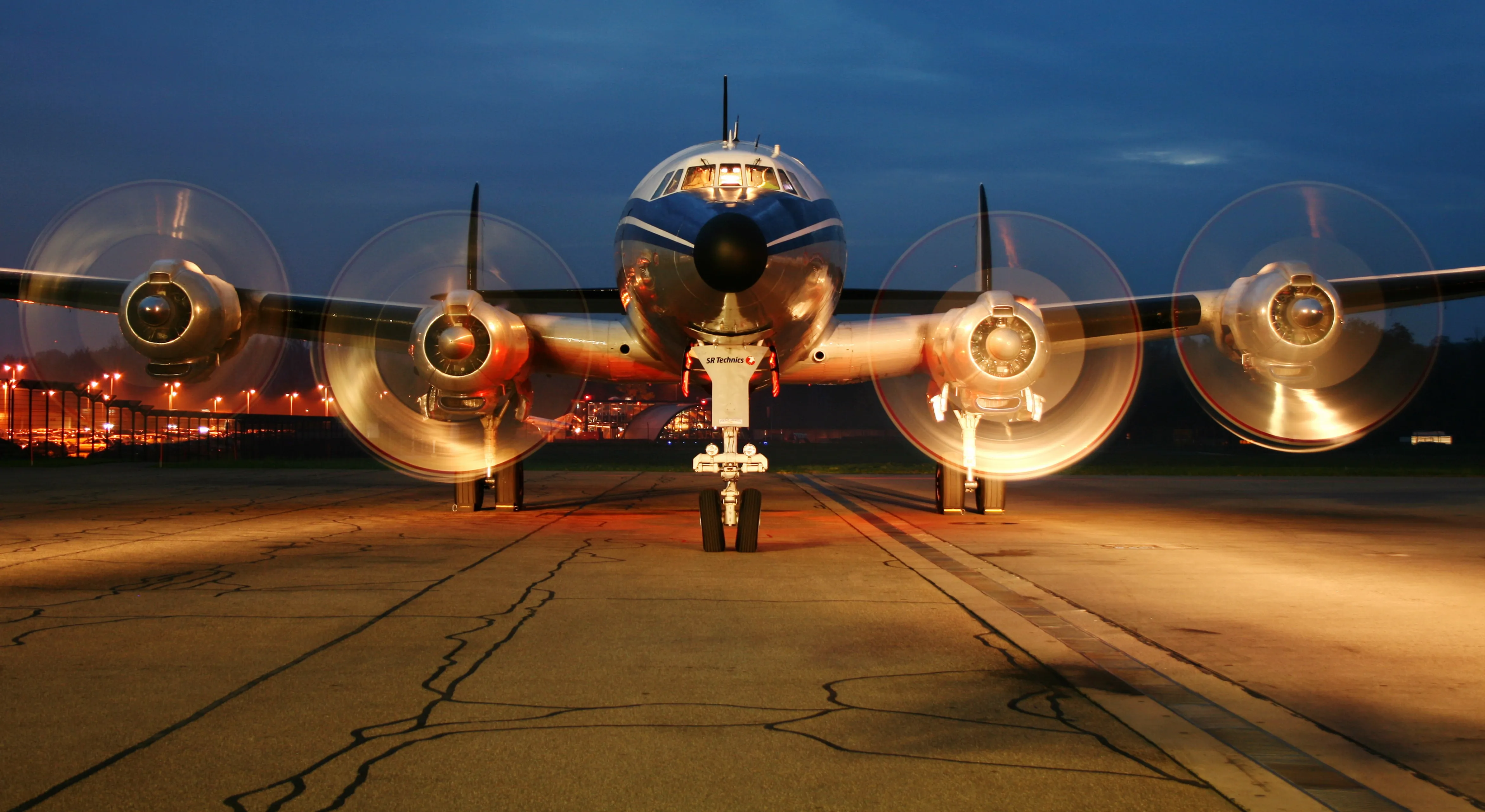 Four engine aircraft on an apron at dusk with airfield lighting behind